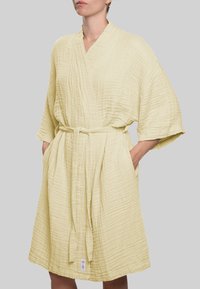 Šviesiai geltonas, tekstūruotas apvyniojamas chalatas su plačiomis rankovėmis, suveržiamu diržu ir šoninėmis kišenėmis. Pagamintas iš minkštos, orui pralaidžios medžiagos, su subtilia dryžuota rašto.