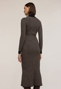 Czarna i beżowa sukienka z prążkowanego dżerseju w paski, z długimi rękawami, wysokim kołnierzem i rozkloszowanym dołem, podkreślająca dopasowany krój.