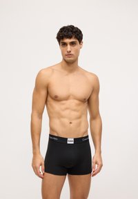 Boxeri negri din bumbac cu un design ajustat, având un logo Calvin Klein alb în contrast pe banda elastică. Textură netedă.