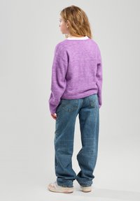 Suéter de lana morado con un corte relajado, combinado con unos jeans de mezclilla azul holgados. Una camiseta blanca asoma por debajo del suéter. Calzado casual.