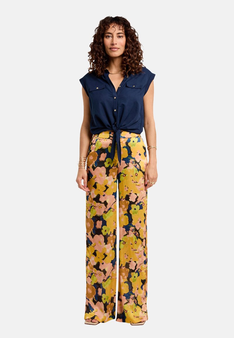 Blusa sin mangas de color navy con botones frontales; pantalones de pierna ancha con estampado floral brillante en amarillo, rosa y azul; detalle anudado en la cintura.