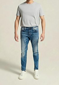 Camiseta gris de manga corta combinada con vaqueros ajustados de mezclilla azul con un acabado desteñido y zapatillas blancas, presentando un look casual.