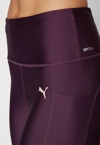 Leggings deportivos de tiro alto en color púrpura, fabricados con tejido que absorbe la humedad, con el logo rosa de Puma y costuras planas para mayor comodidad.