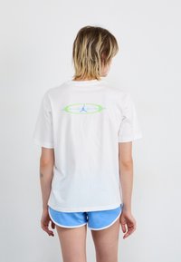 Weißes Baumwoll-T-Shirt mit einem blauen und grünen Jordan-Logo auf der Rückseite, kurzen Ärmeln, lockerer Passform und runden Ausschnitt.