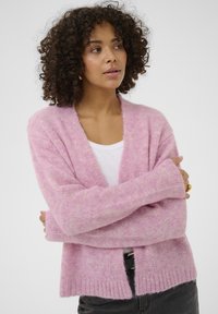 Cardigan rosa chiaro in materiale morbido e strutturato con scollo a V, apertura frontale e orlo a coste. Le maniche lunghe superano i polsi.