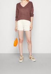 Brun stickad tröja med v-ringning, krämfärgade shorts, orange kviltad handväska och beige sneakers med rosa detaljer. Enkel, avslappnad outfit.