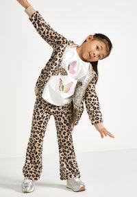 Leopardmønster treningsdrakt med en hvit skjorte med sommerfugltrykk. Sølvfargede sneakers komplementerer antrekket. Myke teksturer, avslappet passform.