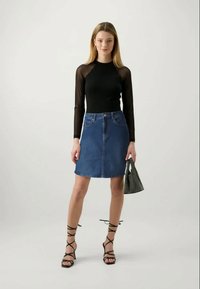 Črna dolga majica z prosojnimi mrežastimi rokavi, v kombinaciji z visokim denim krilom. Model drži teksturirano črno torbico in nosi sandale s trakovi.
