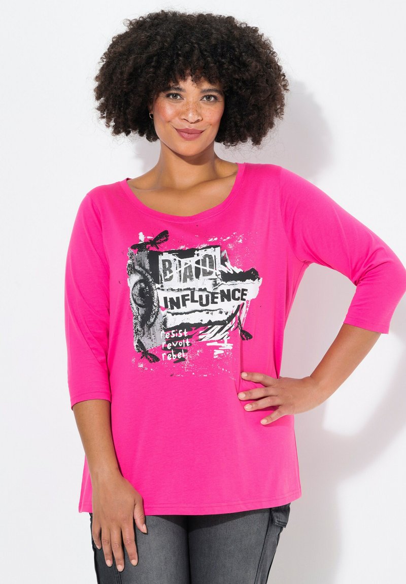 Rosa übergroßes T-Shirt mit 3/4-Ärmeln. Verfügt über einen schwarz-weiß grafischen Druck mit dem Text "Widerstand, Aufstand, Rebellion." Weiche Stofftextur.
