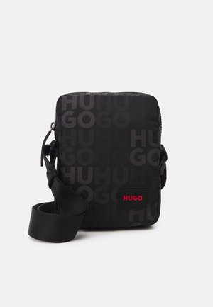 Sac bandoulière noir avec une sangle réglable, un motif de texte embossé "HUGO" et un petit patch logo rouge "HUGO" à l'avant.