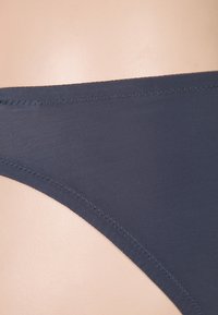 Bas de bikini gris foncé avec une texture lisse, présentant des coutures propres le long des bords et un design minimaliste.