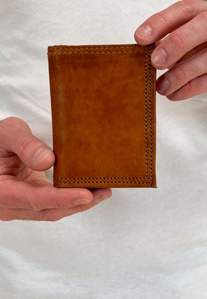 Brown leather wallet with a smooth texture, featuring stitched edges and a vertical orientation, held by hands against a light background.