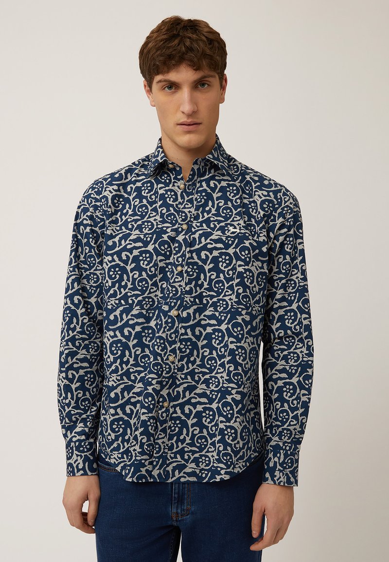 Marineblauwe overhemd met knopen en een wit bloempatroon, lange mouwen en een kraag. De stof lijkt glad met een lichte glans.