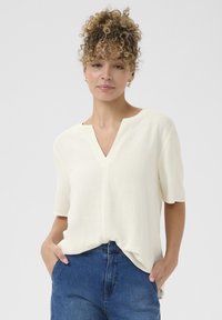 Korte mouwen, V-hals blouse van zachte, off-witte stof. Lichtgewicht textuur met een relaxte pasvorm, met een subtiele naden aan de voorkant en zakken.