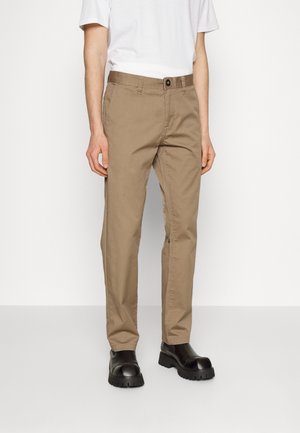 Beige cotton trousers with a straight fit, featuring a button closure and side pockets, worn with black chunky-soled shoes.