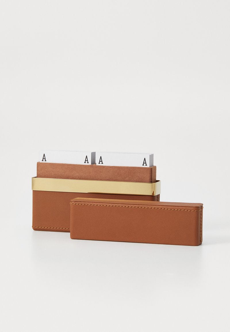 Brown leather card holder with a gold metal band, containing white cards with black lettering. Smooth texture and rectangular shape.