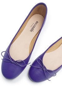 Ballerine in pelle viola con una texture liscia, punta tonda e un fiocco decorativo sulla tomaia. Interno beige con il marchio visibile all'interno.