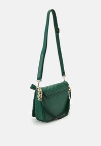 Zielona torebka crossbody z ekoskóry, z pikowanym wzorem, złotymi łańcuszkami, regulowanym paskiem i bocznym zamkiem.