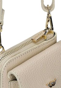 Beige handtas van getextureerd leer met gouden rits, merketiket en gouden gesp bevestigd aan een beige riem.