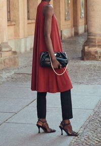 Punainen ilman hihoja oleva mekko, kevyt kangas, levenevä muoto; yhdistetty tiukk fitting mustiin housuihin ja mustiin korkokenkiin, joissa on nauhat; musta clutch-käsilaukku ketjulla.
