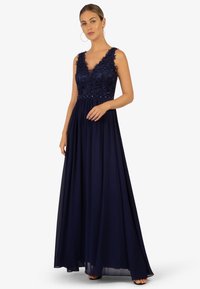 Abito da sera blu navy con busto aderente caratterizzato da dettagli in perline e pizzo, e una gonna fluida. Scollatura a V e design senza maniche.