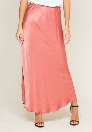 Femme portant une jupe midi en satin corail avec une fente latérale, associée à des talons noirs à bride cheville et un haut blanc rentré.