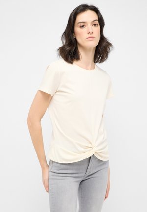 Cream short-sleeve t-shirt with a front twist detail, made of soft fabric. Paired with light grey fitted jeans.