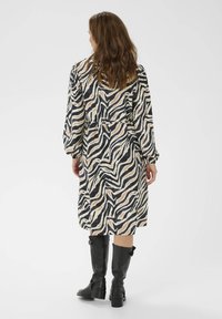 Šaty s dlouhým rukávem v béžovém a černém pruhovaném vzoru zebry, s výrazně staženým pasem. Pod nimi jsou černé kožené kozačky po kolena.