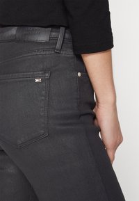 Jeans de mezclilla negra con una textura suave, que presentan un bolsillo trasero, costuras sutiles y una etiqueta de Tommy Hilfiger en la cintura.