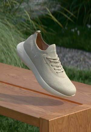 Light beige athletic shoe with a mesh upper, minimalist design, textured surface, and rubber sole, displayed on a wooden surface.