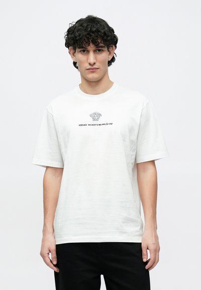Λευκό βαμβακερό T-shirt με γραφική απεικόνιση κεφαλιού Μέδουσας και κείμενο τυπωμένο σε μαύρο χρώμα. Χαλαρή εφαρμογή με κοντά μανίκια και στρογγυλή λαιμόκοψη.