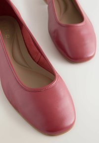 Bailarinas de cuero rojo con punta redonda y textura suave, que presentan un corte bajo y costuras sutiles a lo largo del borde.