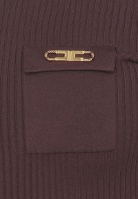 Burgunderfarbiges Strickkleidungsstück mit vertikaler Rippstruktur, einer kleinen Klappentasche und einem Taschenverschluss mit goldfarbener Kette.