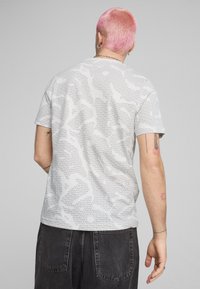 Kortærmet T-shirt i lys grå med et gentagende sort tekstmønster. Har en rund halsudskæring og en afslappet pasform.