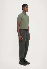 Green short-sleeve polo shirt with embroidered logo; paired with loose-fitting, textured gray sweatpants and black sneakers.