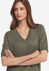 Olivgrön kortärmad V-ringad topp tillverkad av lättstickat tyg. Har ribbade manschetter och halsringning, med en avslappnad passform.