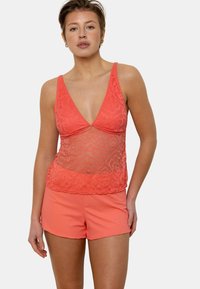 Débardeur en dentelle corail avec un décolleté en V profond et un design transparent, associé à un short corail à côtes assorti. Les deux pièces présentent une texture douce.