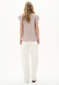 Blusa viola chiaro con maniche a volants, abbinata a pantaloni bianchi a gamba larga. Tessuto morbido, design minimalista, senza motivi o accenti visibili.