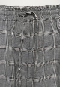 Tissu à carreaux gris et blanc avec une ceinture élastique visible et un cordon noué au centre en haut.