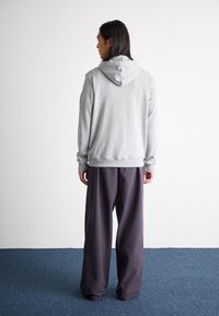 Felpa grigia con cappuccio dal taglio rilassato, abbinata a pantaloni larghi di un viola scuro; design minimalista, texture morbida e senza loghi visibili.