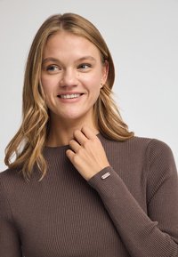 Brun ribbet sweater med høj hals og lange ærmer. Har en lille logo detalje på ærmet. Glat tekstur, afslappet design.