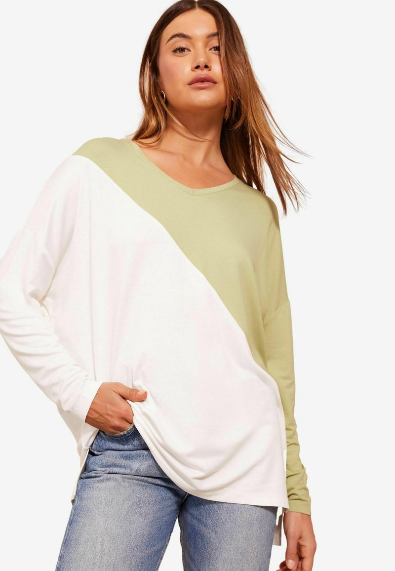 Majica s dolgimi rokavi z diagonalnim razporedom v svetlo zeleni in beli barvi, z dekoltejem v obliki črke V in sproščenim krojem, v kombinaciji z jeans hlačami.
