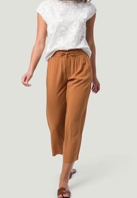Blusa blanca ligera con bordado floral; pantalones cortos de tiro ajustable marrón; la modelo lleva sandalias marrones; texturas suaves y corte relajado.