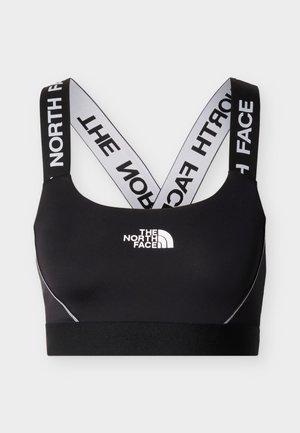 Melns sporta krūšturis ar sakrustotiem baltiem elastīgiem siksnām, uz kurām ir uzraksts "The North Face" un uzņēmuma logotips priekšpusē centrā.
