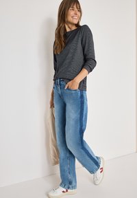 Maglietta grigia scura a maniche lunghe, jeans azzurri a vestibilità rilassata con pannelli laterali più scuri e sneakers bianche con accenti rossi. Texture liscia.