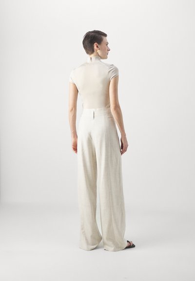 Ανοιχτό μπεζ εφαρμοστό τοπ με κοντά μανίκια, συνδυασμένο με ψηλόμεσες, φαρδιές παντελόνες από λινό σε ελαφρύτερο μπεζ, που αποδεικνύουν λεία υφή.