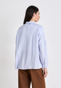 Lichtblauwe langemouwen shirt met een gestructureerd gestreept patroon, met knoopmanchetten en een relaxte pasvorm, gecombineerd met een paar bruine broek.