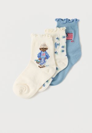 Three ankle socks with ruffled edges: cream sock with bear in blue outfit, cream sock with blue flowers, and blue sock with American flag.