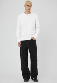 Chemise blanche à manches longues associée à un jean noir ample et à des chaussures noires. La chemise a un col rond et des manches à revers.