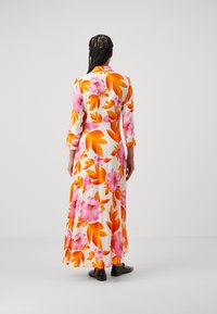 Abito lungo floreale con vivaci motivi arancioni e rosa su sfondo bianco. Maniche a tre quarti e una silhouette fluida.